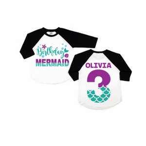 May include: A white and black baseball tee shirt with the text "Birthday Mermaid" on the front and a purple number "3" with teal mermaid scales on the back. The name "Olivia" is printed above the number.