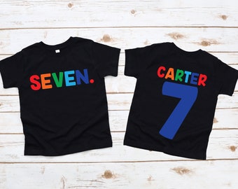 May include: Two black t-shirts with rainbow lettering. The front shirt says "SEVEN." The back shirt says "CARTER" with a large blue number "7" underneath.