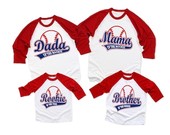 May include: Four baseball-themed shirts with red and white sleeves. The shirts say "Dada of the Rookie", "Mama of the Rookie", "Rookie of the Year", and "Brother of the Rookie".