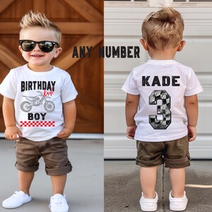 Puede incluir: Una camiseta blanca con un gr&aacute;fico de motocicleta y las palabras "BIRTHDAY BOY" en negro. El nombre "Kade" est&aacute; en rojo. La parte posterior de la camiseta tiene el nombre "KADE" y el n&uacute;mero "3" en un patr&oacute;n de tablero de ajedrez. El ni&ntilde;o lleva pantalones cortos marrones y zapatillas blancas.