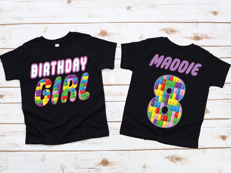 May include: Two black t-shirts with a birthday theme. One shirt says "Birthday Girl" in pink letters with a colourful Lego design. The other shirt has the name "Maddie" in pink letters and a large number "8" made of colourful Lego blocks.
