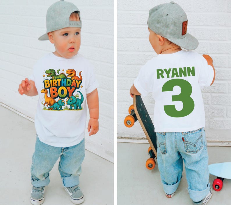 May include: A toddler wearing a white t-shirt with a colorful dinosaur graphic and the text "BIRTHDAY BOY". The child is also wearing blue jeans and a gray baseball cap. The back of the shirt has the name "RYANN" and the number "3".
