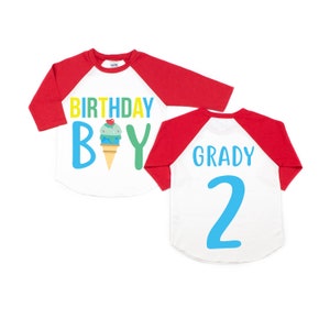 May include: Red and white baseball style shirt with a blue and green ice cream cone graphic and the text "Birthday Boy". The back of the shirt has the name "Grady" and the number "2" in blue.