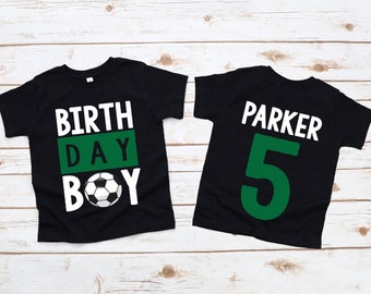 May include: Two black t-shirts with white text and a green soccer ball graphic. The first shirt says "BIRTH DAY BOY" with a soccer ball in the middle. The second shirt says "PARKER 5" in white text.
