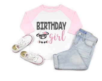May include: A white and pink long-sleeved shirt with a pink and white baseball style design. The shirt has the text "Birthday girl" in pink and black lettering with a cartoon lamb wearing a flower crown.