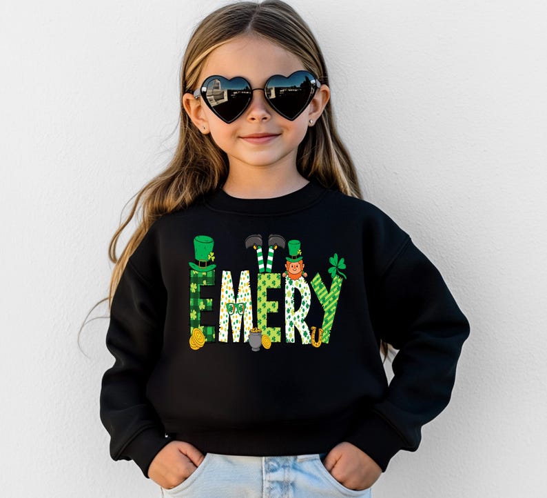 May include: Black sweatshirt with a green, white, and gold design of leprechauns and shamrocks spelling out the name "EMERY".