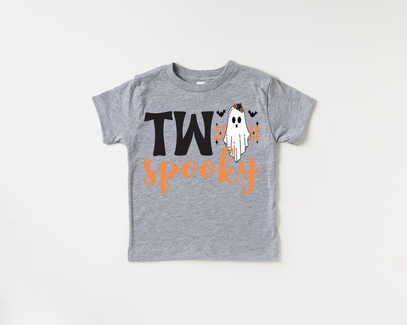 Pu&ograve; includere: Una maglietta grigia a maniche corte con le parole "TWo Spooky" in nero e arancione. Un fantasma bianco con un cappello nero e dettagli arancioni &egrave; a destra del testo. Piccoli pipistrelli neri e dettagli arancioni completano il design di Halloween.