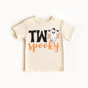 Pu&ograve; includere: T-shirt color crema per bambini piccoli con le parole "TW" in nero e "spooky" in arancione. Un fantasma dei cartoni animati con una fascia floreale e pipistrelli &egrave; stampato sulla maglietta, perfetto per Halloween.