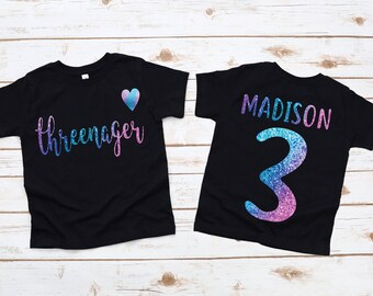 May include: Two black t-shirts with a glittery design. One shirt says "three-nager" with a pink and blue heart. The other shirt says "MADISON" with the number "3" in glittery pink and blue.