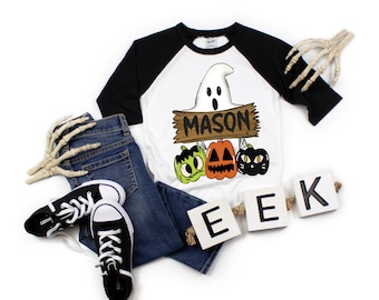 May include: A Halloween-themed outfit featuring a white and black raglan shirt with a ghost and pumpkin graphic, the name "MASON", and the word "EEK". The outfit includes blue jeans and black sneakers. Decorative skeleton hands are also present.