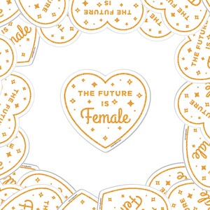 May include: A white heart-shaped sticker with gold glitter and the text "The Future is Female" in a gold glitter font.
