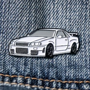 May include: White enamel pin of a Nissan Skyline R34, a popular Japanese sports car.