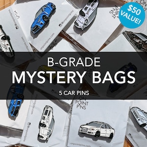 May include: Five car-themed enamel pins in a mystery bag. The bag is labeled "B-Grade Mystery Bags" and "5 Car Pins". The pins are in various colors, including blue, white, and yellow. The bag is on a table with other similar bags.