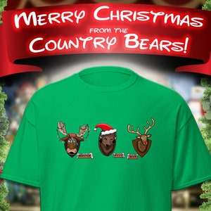 May include: Green t-shirt with a Christmas-themed design featuring three Country Bear Jamboree characters:  a moose with Christmas lights, a bear wearing a Santa hat, and a reindeer. The text "Merry Christmas from the Country Bears!" is displayed above the characters.