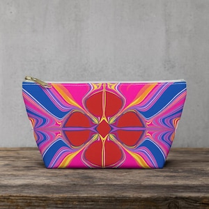 Peut inclure: Une trousse zippée aux couleurs vives avec un motif abstrait saisissant. Le motif présente un motif floral rouge central entouré de lignes bleues, roses, jaunes et oranges tourbillonnantes. La trousse a une fermeture éclair dorée.