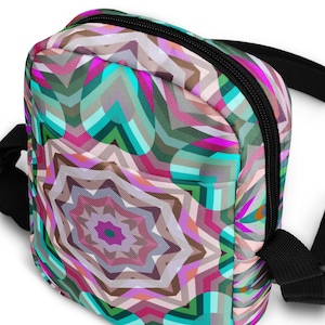 May include: A small, colorful bag with a geometric pattern in shades of pink, teal, and brown. The bag has a black zipper and a black strap. The design features a central starburst shape.
