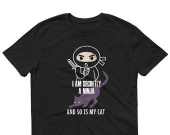 Op de afbeelding: Zwart t-shirt met een witte ninja-afbeelding met een zwaard en een vinger voor de lippen. Daaronder een paarse kat. De tekst luidt: "I AM SECRETLY A NINJA AND SO IS MY CAT."