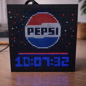 May include: Black LED clock displaying the Pepsi logo in red, white, and blue. The time 10:07:32 is shown in blue. The clock is on a wooden surface.