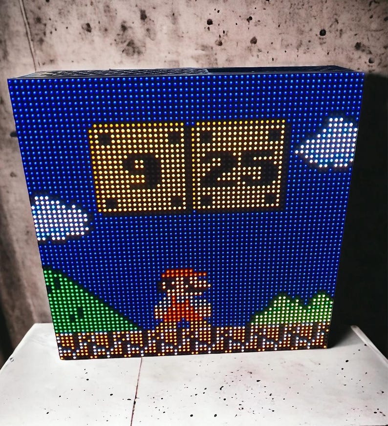 May include: A blue LED light box with a pixelated design of a classic video game scene. The scene includes a character, a score of 325, clouds, and a green landscape. The box is illuminated with small, bright lights.