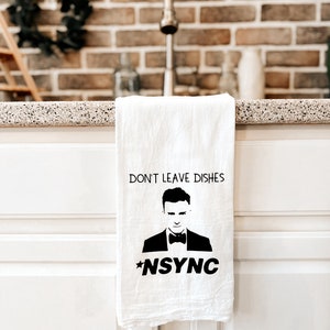 May include: White kitchen towel with a black silhouette of a man wearing a tuxedo and bow tie. The text "DON'T LEAVE DISHES *NSYNC" is printed on the towel.