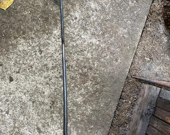 May include: A long, hand-forged iron fire poker with a dark gray finish. The tool features a straight, slender shaft that terminates in a decorative, curled loop handle at one end and a sharp, angled hook at the opposite end for moving logs.
