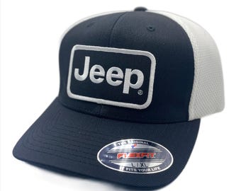 May include: A black and white Jeep baseball cap with a curved brim. The front of the cap features a rectangular patch with the word "Jeep" in white lettering. The back of the cap is white mesh. The cap has a Flexfit sticker.
