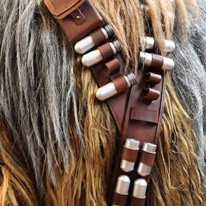 May include: A brown leather bandolier with multiple silver canisters attached. The bandolier has a small brown leather pouch on the shoulder strap.