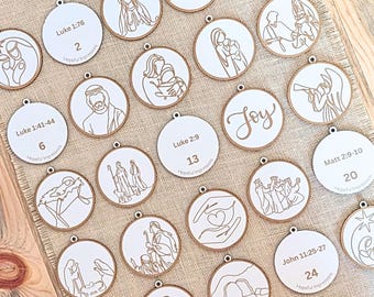 May include: A selection of circular white ornaments with a wooden edge. Each ornament displays a religious illustration and scripture reference in a minimalist style. One ornament has the word "Joy". The ornaments are arranged on a beige fabric surface.