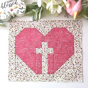 May include: A pink heart-shaped quilt block with a white background and a floral pattern. The heart is made up of smaller squares with different floral patterns and the words "Primrose", "Rose", "Lavender", "Bluebell", "Petunia", "Dahlia", "Lily", "Violet", "Iris", "Anemone", "Sunflower", "Peony", and "Mrose" written on them.