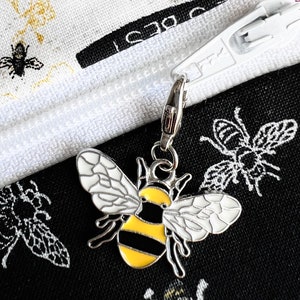 May include: A silver zipper charm with a black and yellow bee design. The bee has white wings and a yellow and black striped body.