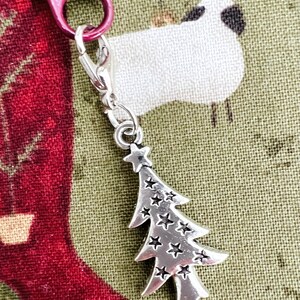 May include: A silver charm in the shape of a Christmas tree with stars. The charm is attached to a red zipper pull with the word "YKK" on it.