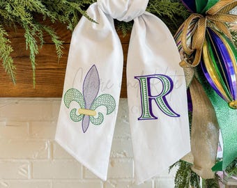 May include: White fabric scarf with a purple and green fleur-de-lis on one side and a purple letter "R" on the other side.