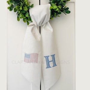 May include: A white fabric door swag with a blue and red American flag and a blue embroidered letter "H" on it.