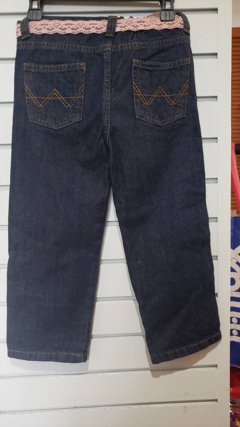 May include: Dark blue denim jeans with a pink lace waistband and brown stitching on the back pockets.