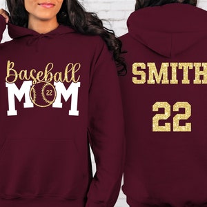 May include: Burgundy hooded sweatshirt with the text "Baseball Mom" in white with a gold baseball graphic. The back of the sweatshirt has the text "SMITH 22" in gold.