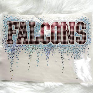 May include: A white fabric patch with the word "FALCONS" spelled out in dark red rhinestones. The word is outlined with clear rhinestones, and additional rhinestones cascade down the patch.