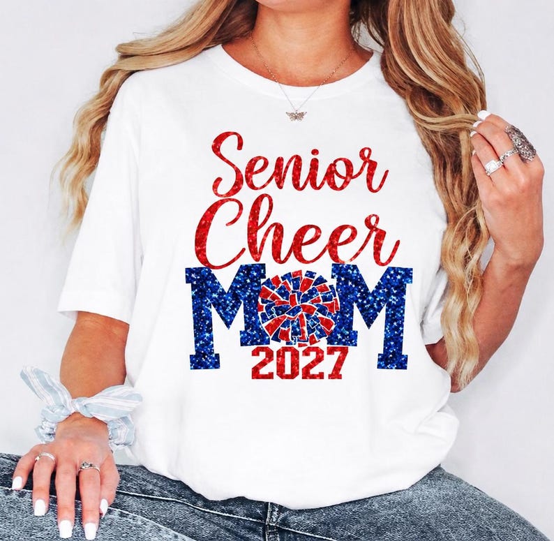 May include: White t-shirt with the text "Senior Cheer Mom 2027" in red and blue glitter. The design includes a cheerleader pom-pom graphic. A perfect gift for a cheerleading mom.
