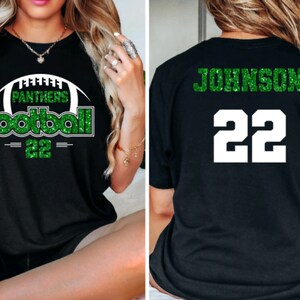 May include: Black t-shirt with green glitter text and a football graphic. The front of the shirt says "Panthers Football 22". The back of the shirt says "Johnson 22".