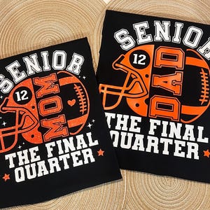 May include: Two black t-shirts featuring orange football helmet graphics with the number 12. One shirt reads SENIOR MOM and the other SENIOR DAD, both with the text THE FINAL QUARTER in white block letters and small star accents.