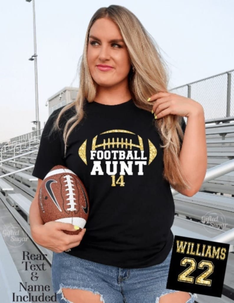 May include: Black t-shirt with gold glitter football design and the text "Football Aunt 14". A brown football is held in the left hand of the person wearing the shirt. A gold glitter jersey patch with the text "Williams 22" is in the lower right corner of the image.