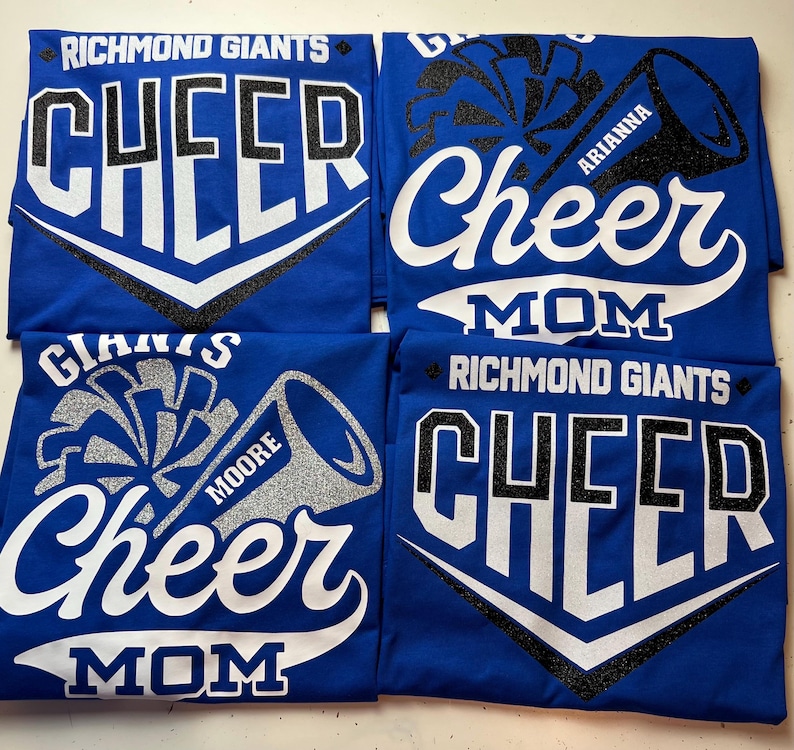 May include: Four royal blue t-shirts with white and black glitter text that reads "Richmond Giants Cheer" and "Cheer Mom". The shirts feature a white and black glitter cheerleading pom-pom and megaphone graphic. The megaphones have the names "Moore", "Arianne", and "Mom" written on them.
