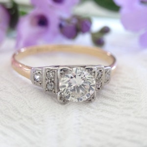 May include: A vintage engagement ring with a large, round, clear diamond center stone. The ring is set in platinum with a yellow gold band and features smaller diamonds on the sides.
