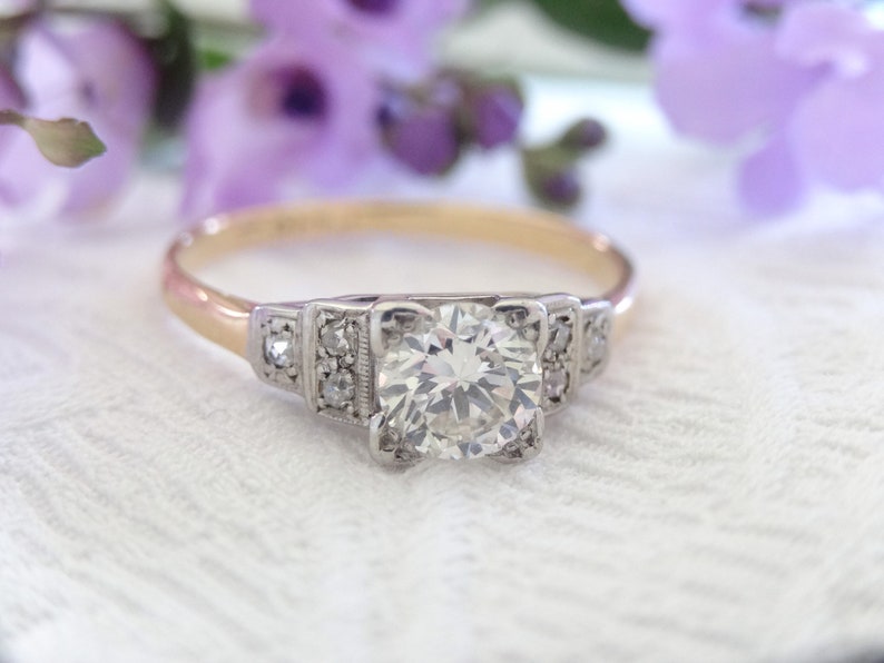 May include: A vintage engagement ring with a large, round, clear diamond center stone. The ring is set in platinum with a yellow gold band and features smaller diamonds on the sides.