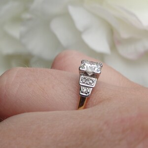 May include: A silver engagement ring with a large, round, clear diamond center stone and smaller diamonds on the band. The ring is on a finger.