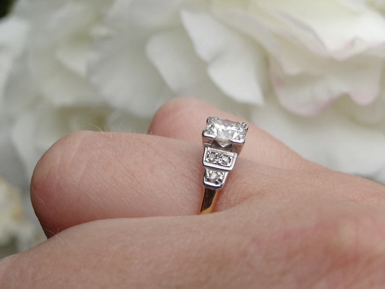 May include: A silver engagement ring with a large, round, clear diamond center stone and smaller diamonds on the band. The ring is on a finger.