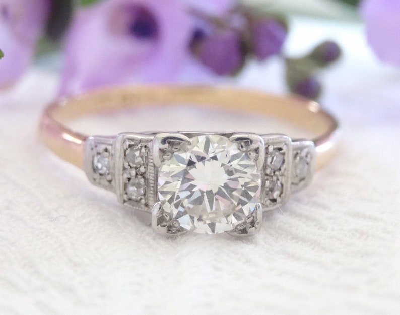 May include: A vintage engagement ring with a large, round, brilliant-cut diamond set in a platinum band. The band is accented with smaller diamonds on either side of the center stone.