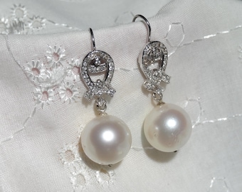 May include: A pair of silver-toned drop earrings featuring large, round, white pearls suspended from a decorative, horseshoe-shaped metal setting encrusted with small, clear, sparkling stones and secured with curved ear wires.