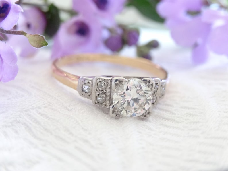 May include: A vintage engagement ring with a large, round, brilliant-cut diamond set in a platinum band. The ring has a delicate, Art Deco-inspired design with small diamonds on the sides.
