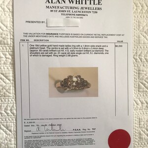 May include: A yellow gold ladies ring with a platinum head. The center of the ring has a large, brilliant cut diamond. The shoulders of the ring are set with six smaller diamonds. The ring weighs 2.68 grams.  F.G.A.A. Reg No. T07