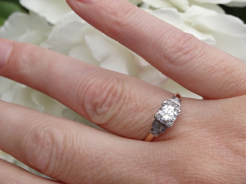 May include: A gold band engagement ring with a large, round, clear diamond center stone and smaller diamonds on the band.